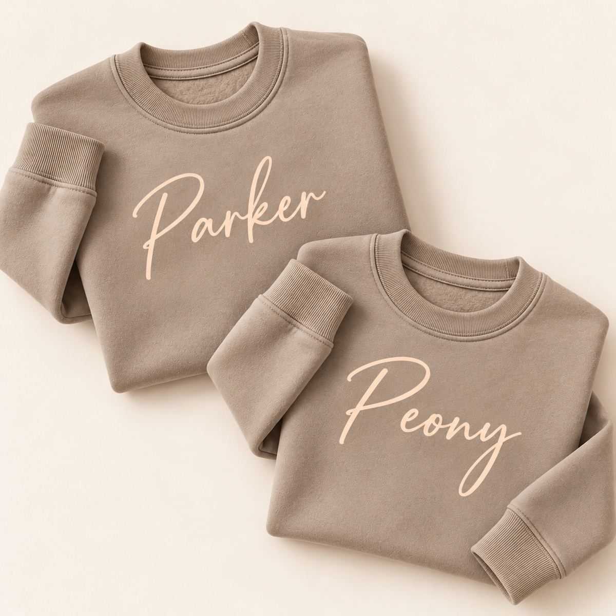 Two personalised mink sweatshirts with cream script names, folded on a beige background | Grace & Grayson”ink