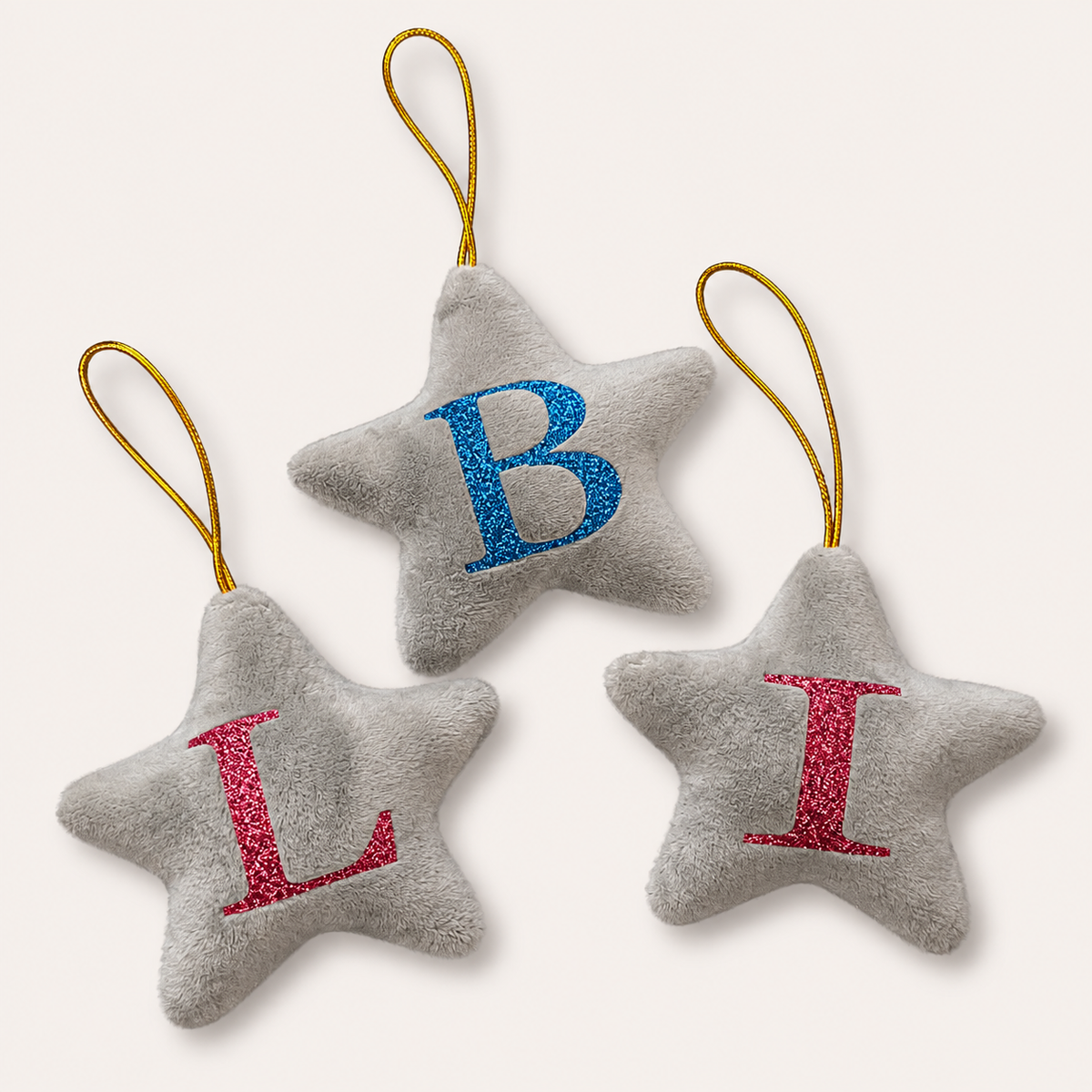 Three grey personalised initial Christmas star tree decorations with blue, pink and red glitter lettering, displayed together, Grace & Grayson