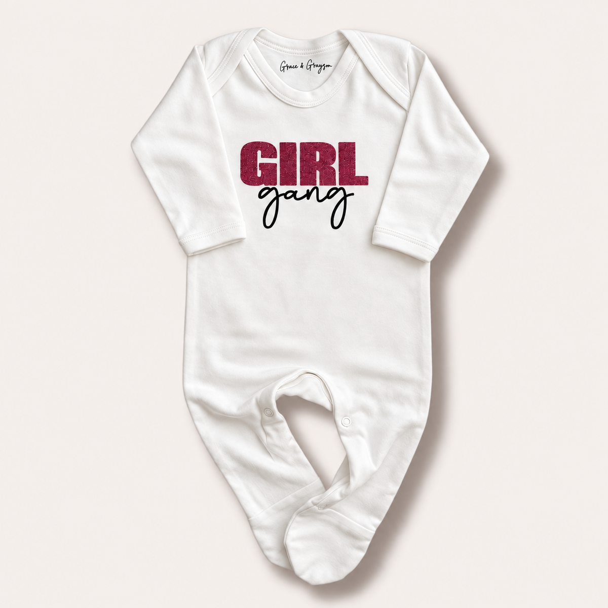 White long-sleeve Girl Gang baby grow laid flat showing the pink glitter and black front design, Grace & Grayson
