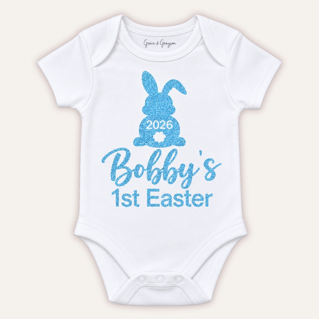 White personalised 1st Easter baby vest with a blue glitter bunny design and 2026 detail, Grace & Grayson