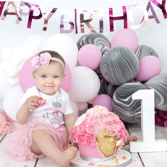 Baby girl wearing personalised birthday tutu set with pink tutu and silver glitter crown design at 1st birthday cake smash - Grace & Grayson
