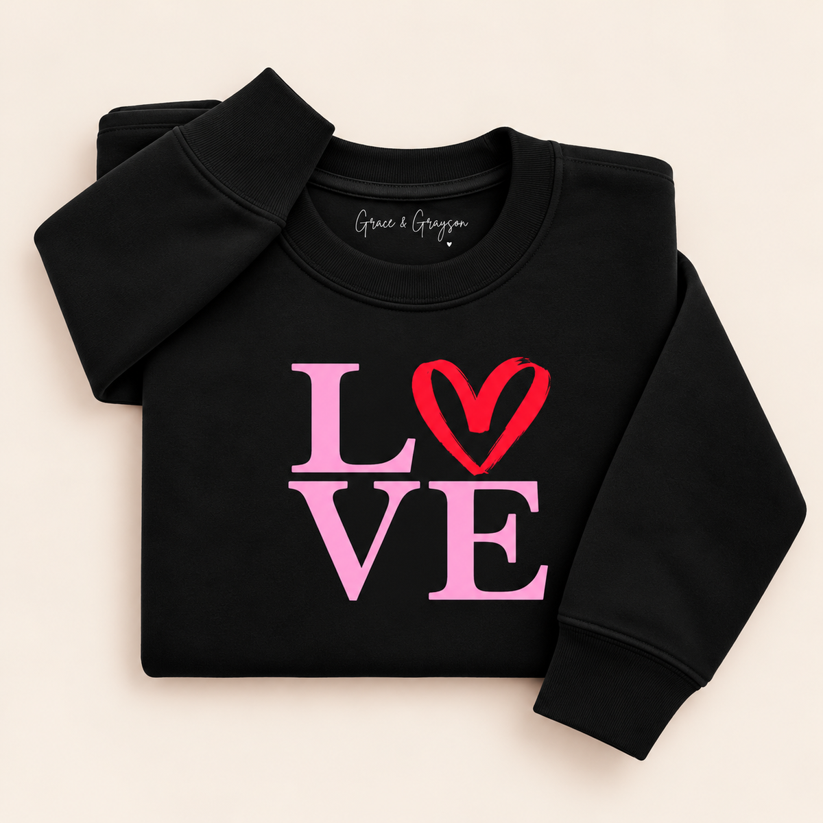 Black sweatshirt with pink LOVE lettering and a red heart replacing the O, folded on a cream background | Grace & Grayson