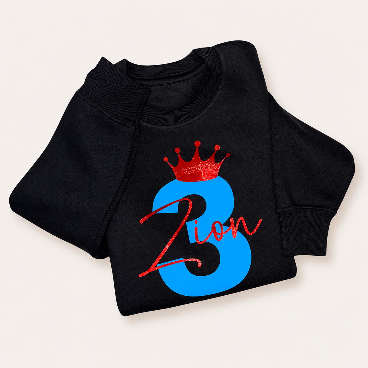 Black personalised birthday sweatshirt with a blue number 3, red crown and red script name, folded on a white background | Grace & Grayson