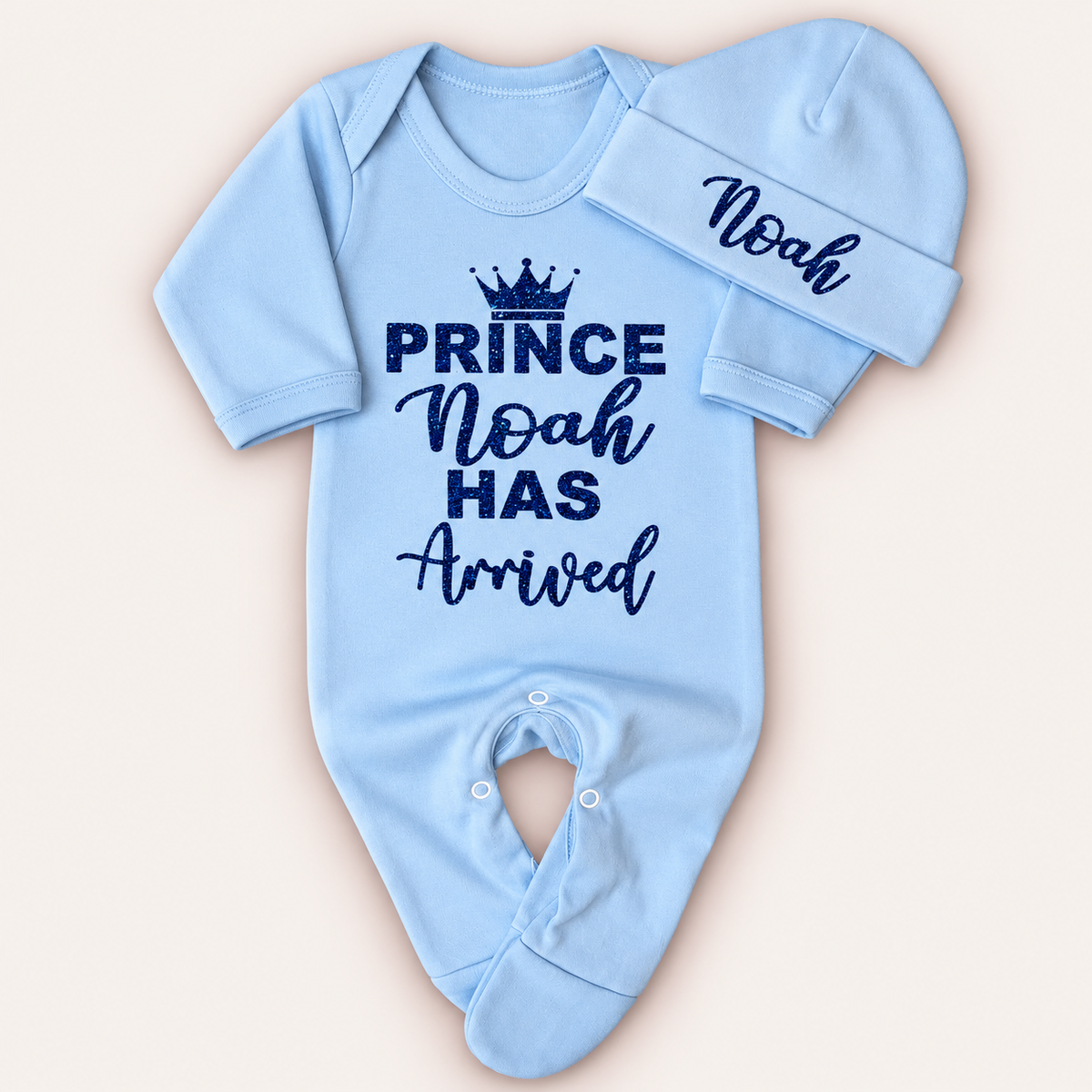 Blue personalised Prince Has Arrived baby grow and matching hat with a navy glitter crown design, Grace & Grayson