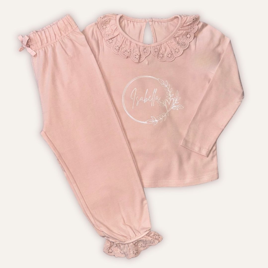 Blush pink personalised broderie frill pyjamas with a silver wreath design, laid flat, Grace & Grayson