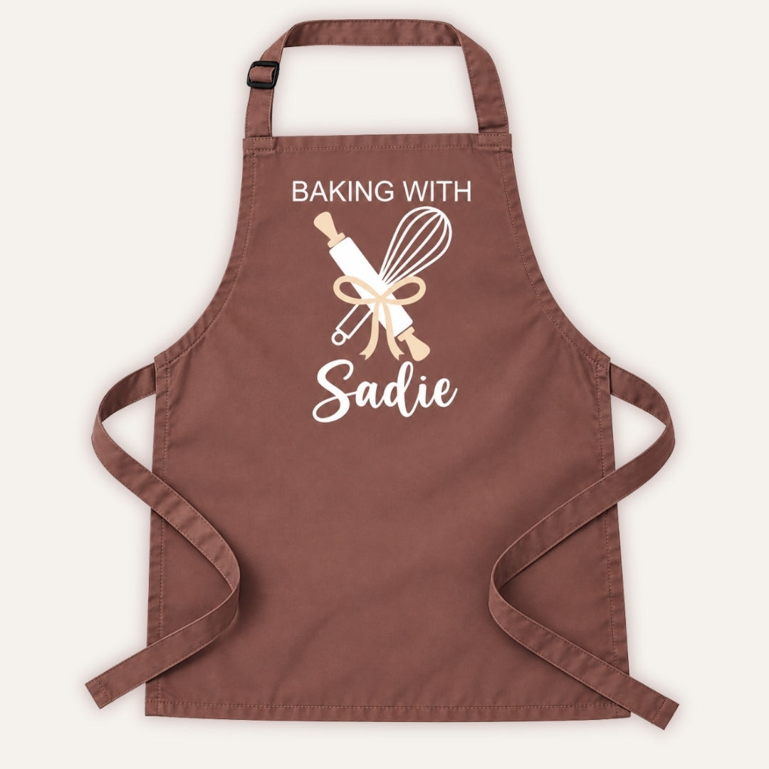 Brown personalised adult baking apron with “Baking With” text, rolling pin and whisk design on a white background, Grace & Grayson