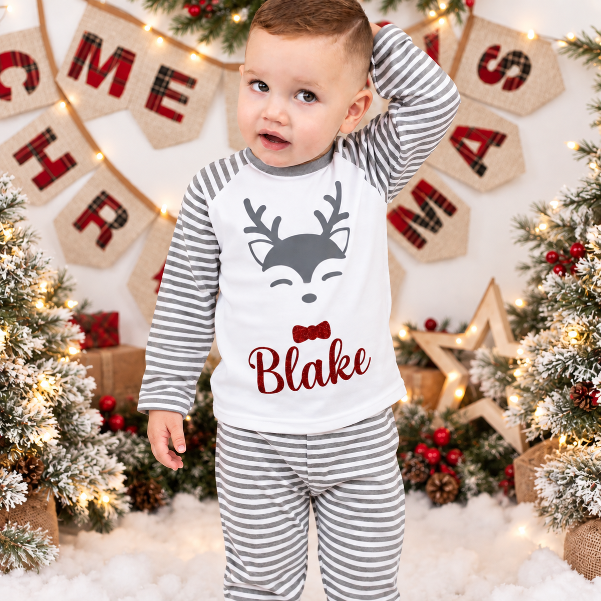 Child wearing personalised grey stripe Christmas reindeer pyjamas in a festive Christmas setting, Grace & Grayson