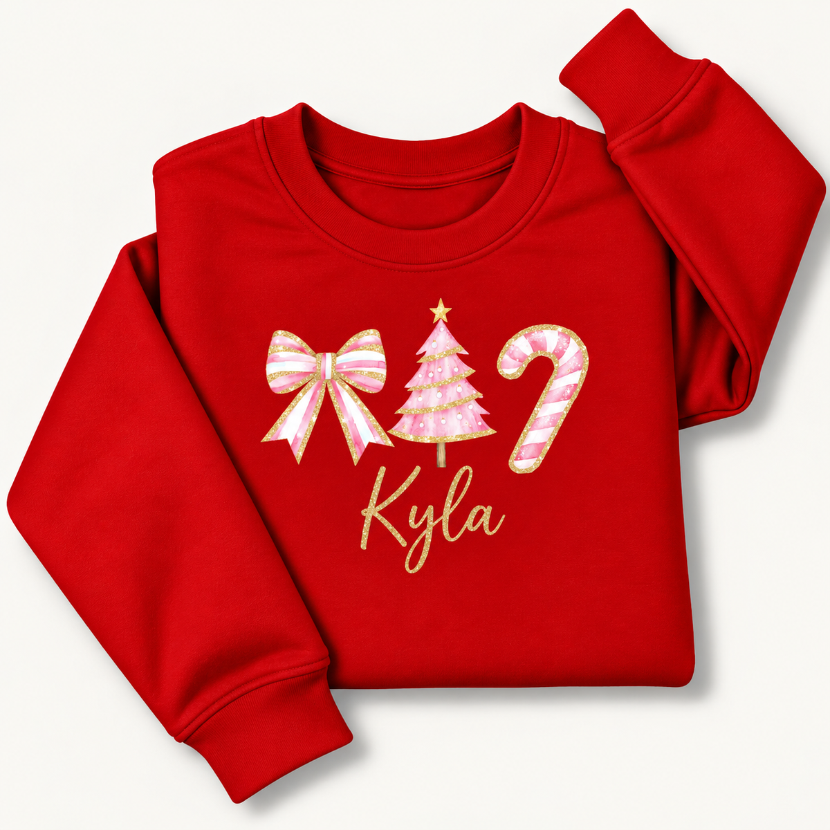 Red personalised Christmas sweatshirt with a pink bow, Christmas tree and candy cane, gold detailing and script name, folded on a cream background | Grace & Grayson