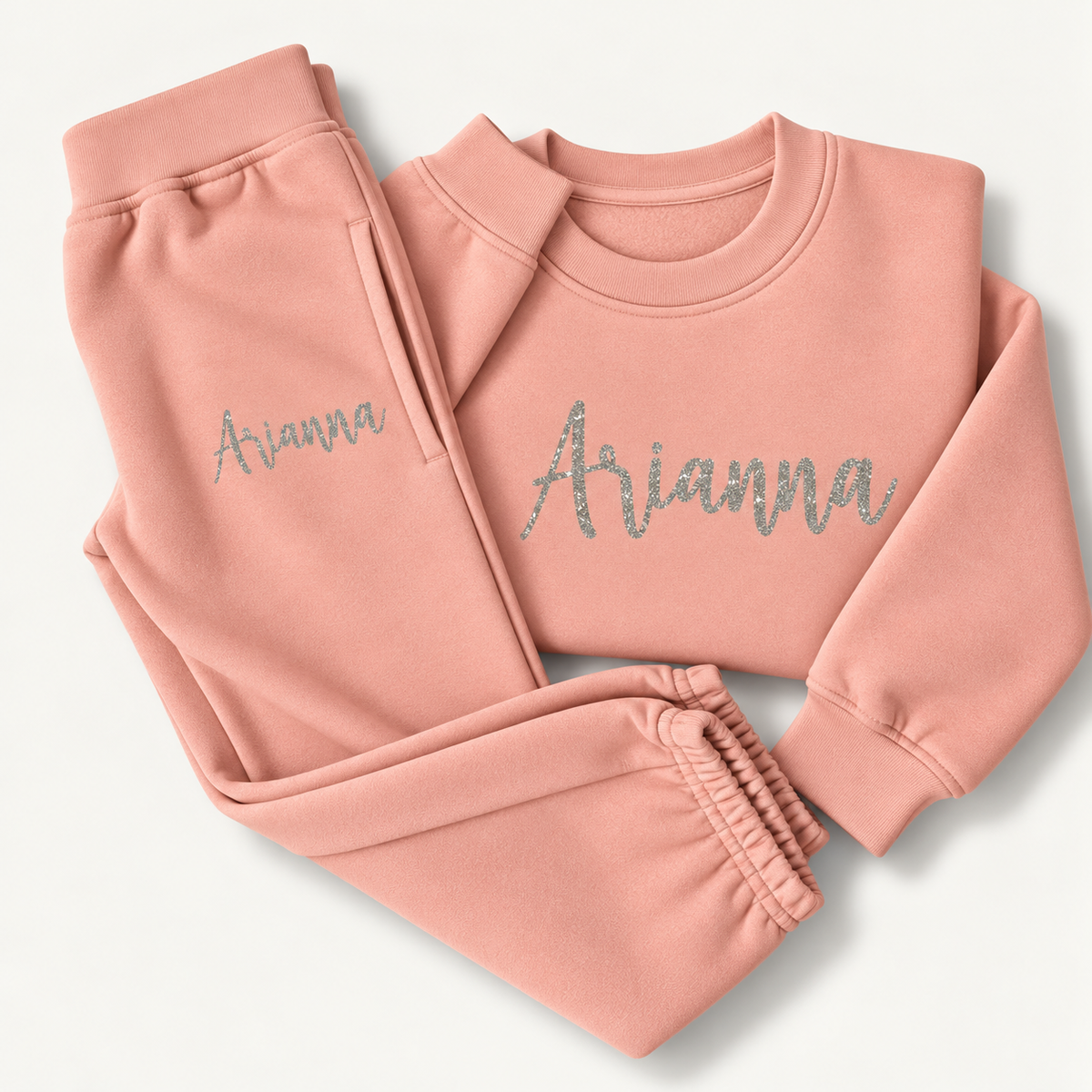 Dusty pink personalised loungewear set laid flat with a silver glitter script name across the sweatshirt chest and on the joggers, Grace & Grayson