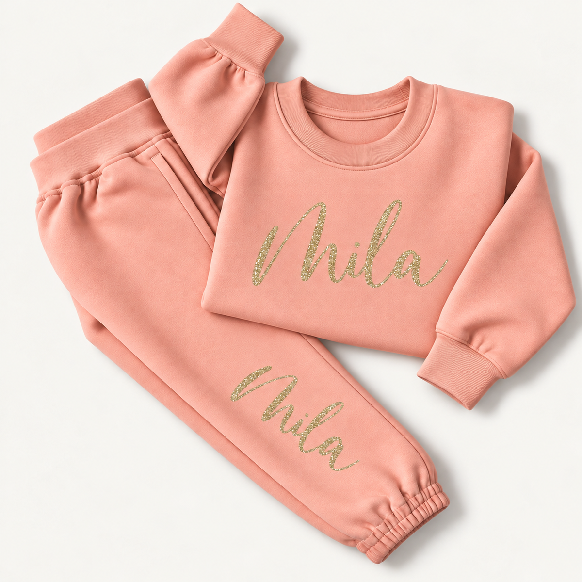 Dusty pink personalised sweatshirt and joggers laid flat with a gold glitter script name across the chest and down the leg, Grace & Grayson
