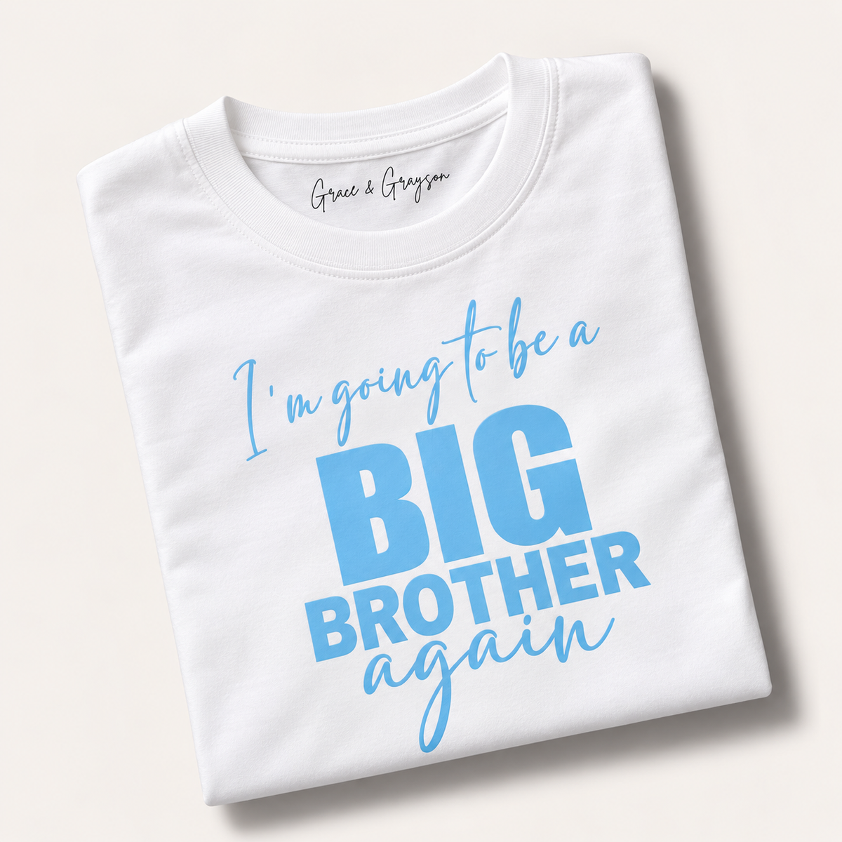 Folded white personalised “I’m Going to Be a Big Brother Again” t-shirt in blue lettering, Grace & Grayson.