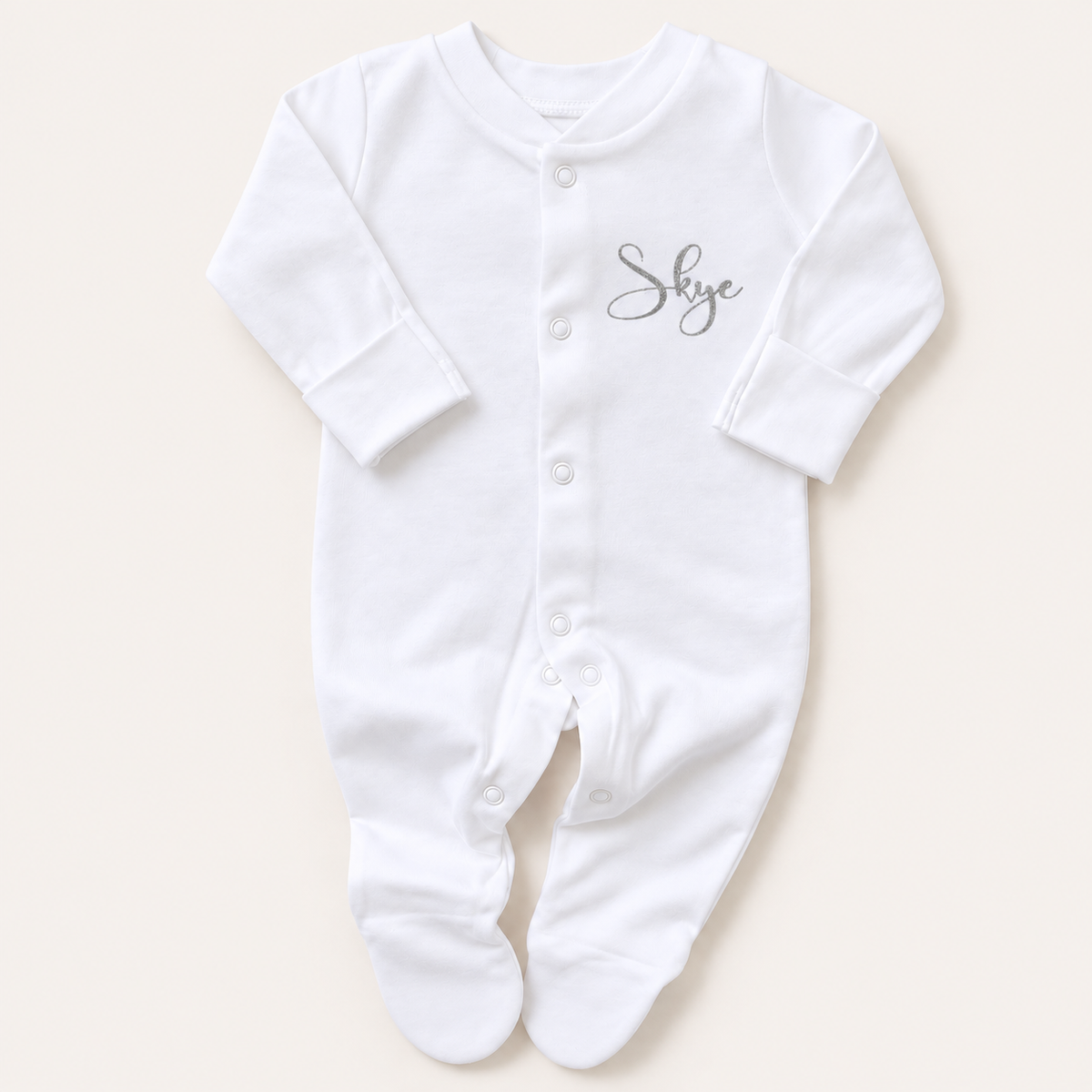 Front view of a white footed baby grow with a small personalised name on the chest, button fastening and long sleeves, Grace & Grayson