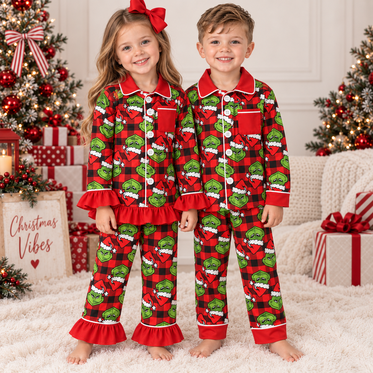 Girl and boy wearing personalised red, black & green Grinch Christmas pyjamas, with frill details on the girl’s set, in a festive Christmas setting by Grace & Grayson