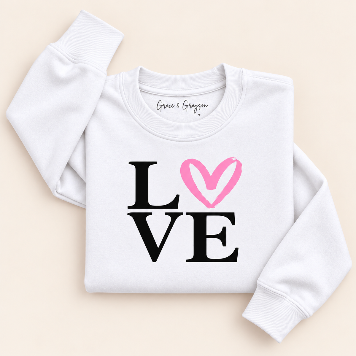 White sweatshirt with black LOVE lettering and a pink heart replacing the O, folded on a cream background | Grace & Grayson