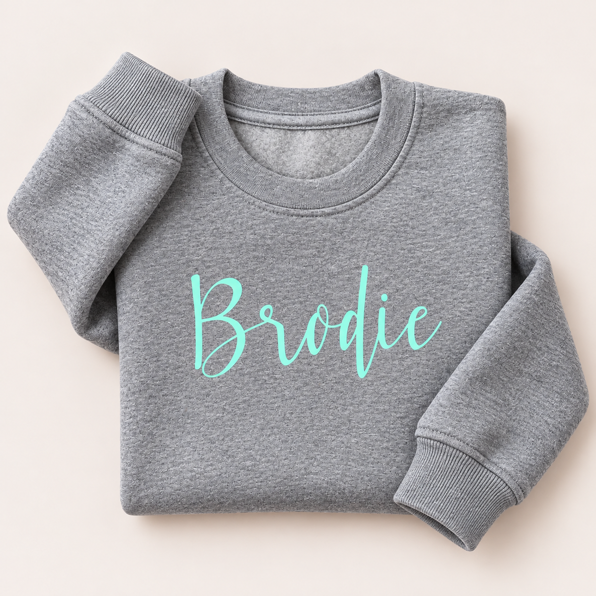 Grey marl personalised sweatshirt with a mint green script name across the chest, folded on a beige background | Grace & Grayson