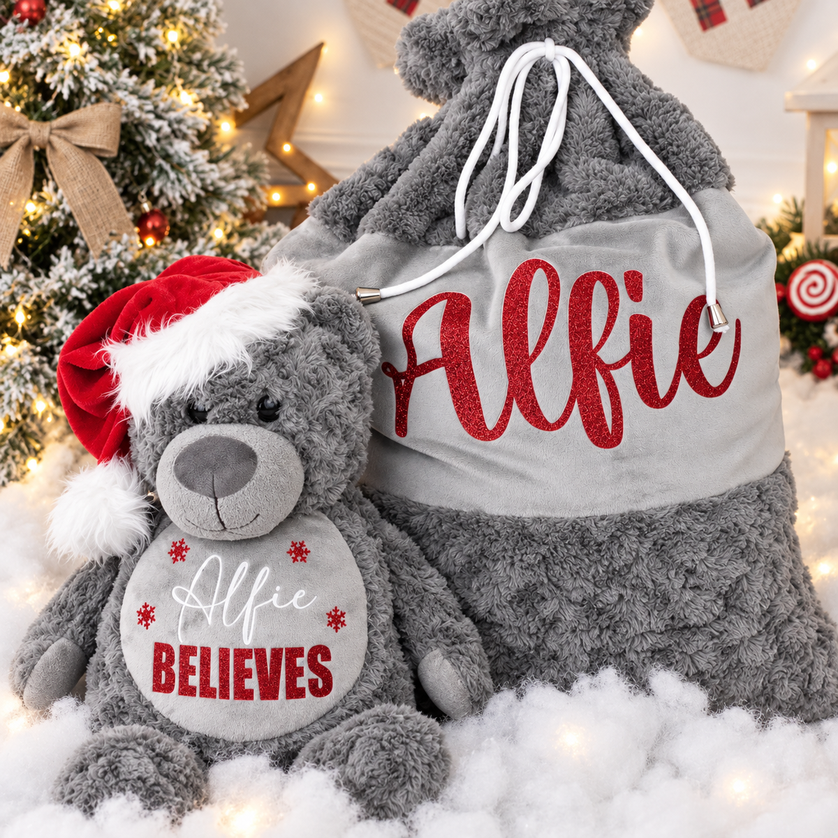 Grey personalised Believes Christmas teddy wearing a Santa hat beside a matching Christmas sack and Christmas tree, Grace & Grayson