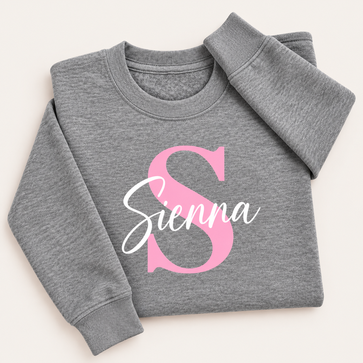 Grey personalised sweatshirt with a pink initial and white script name, laid flat | Grace & Grayson