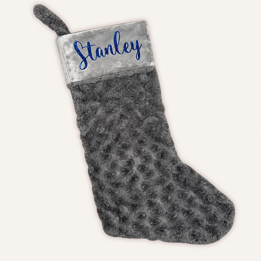 Grey plush Christmas stocking with a grey cuff, blue glitter personalised lettering and a hanging loop, Grace & Grayson.