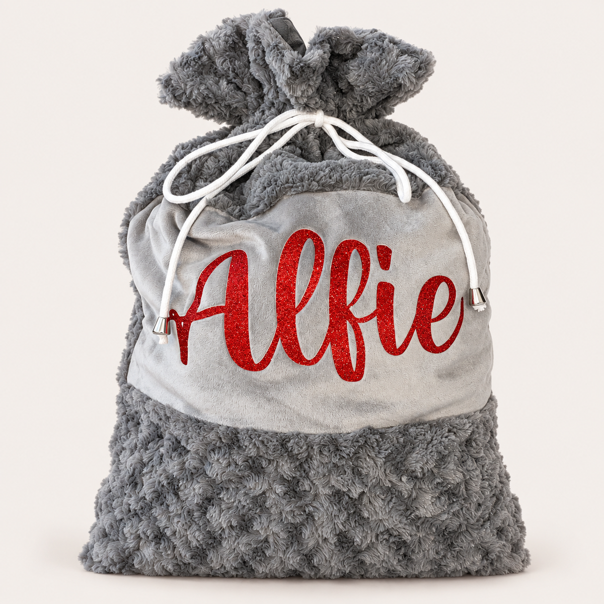 Grey plush personalised Christmas Santa sack with red glitter name lettering and white drawstrings against a light background, Grace & Grayson.