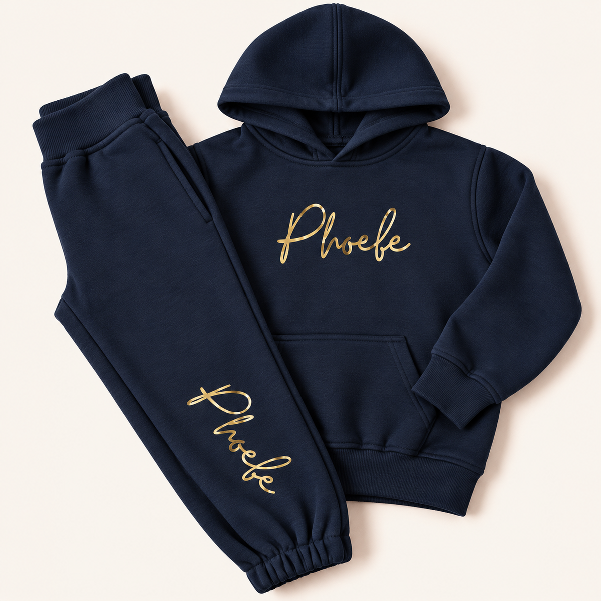 Navy personalised hoodie tracksuit laid flat with a gold script name on the hoodie chest and down the jogger leg, Grace & Grayson