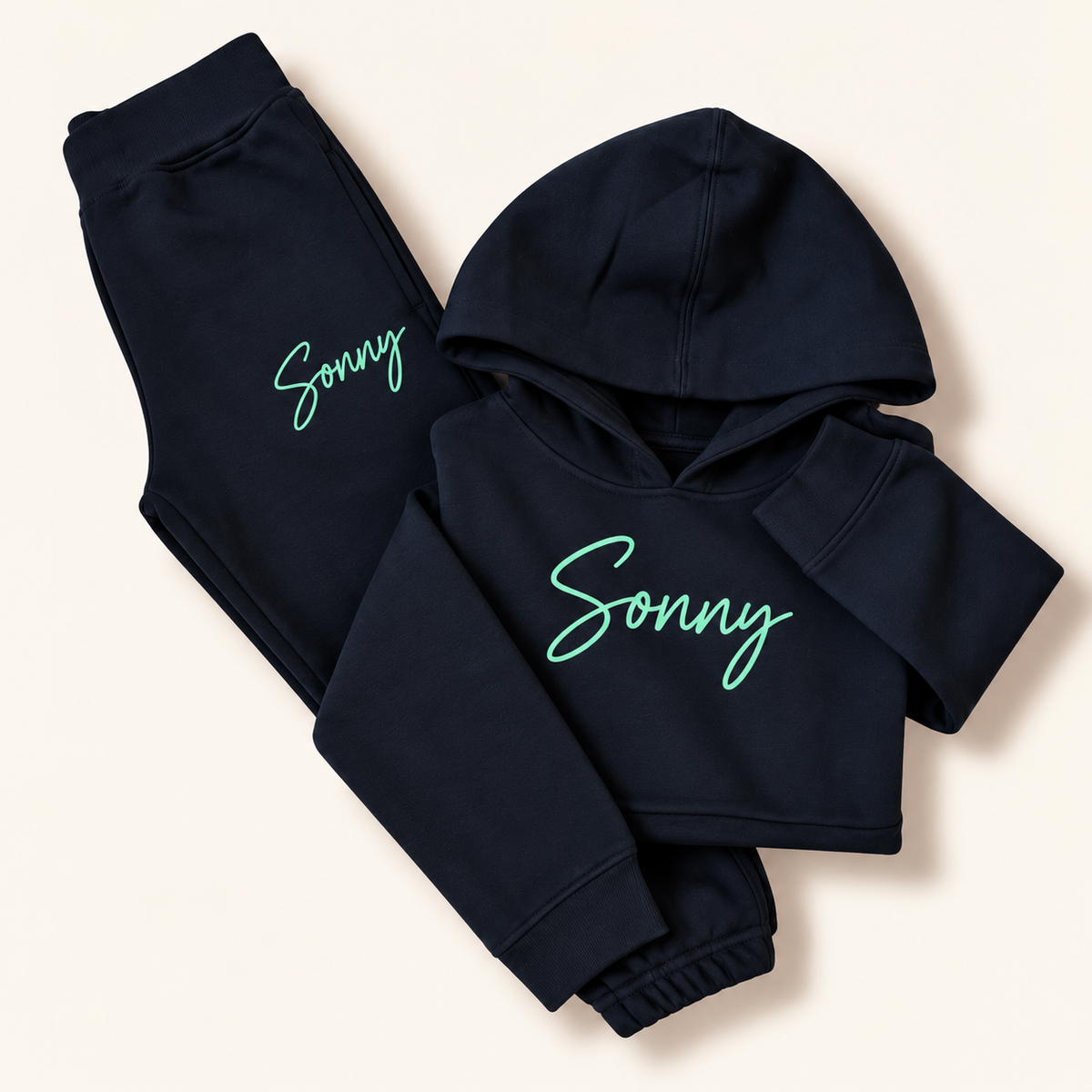 Navy personalised hoodie tracksuit laid flat with a mint green script name on the hoodie chest and joggers, Grace & Grayson