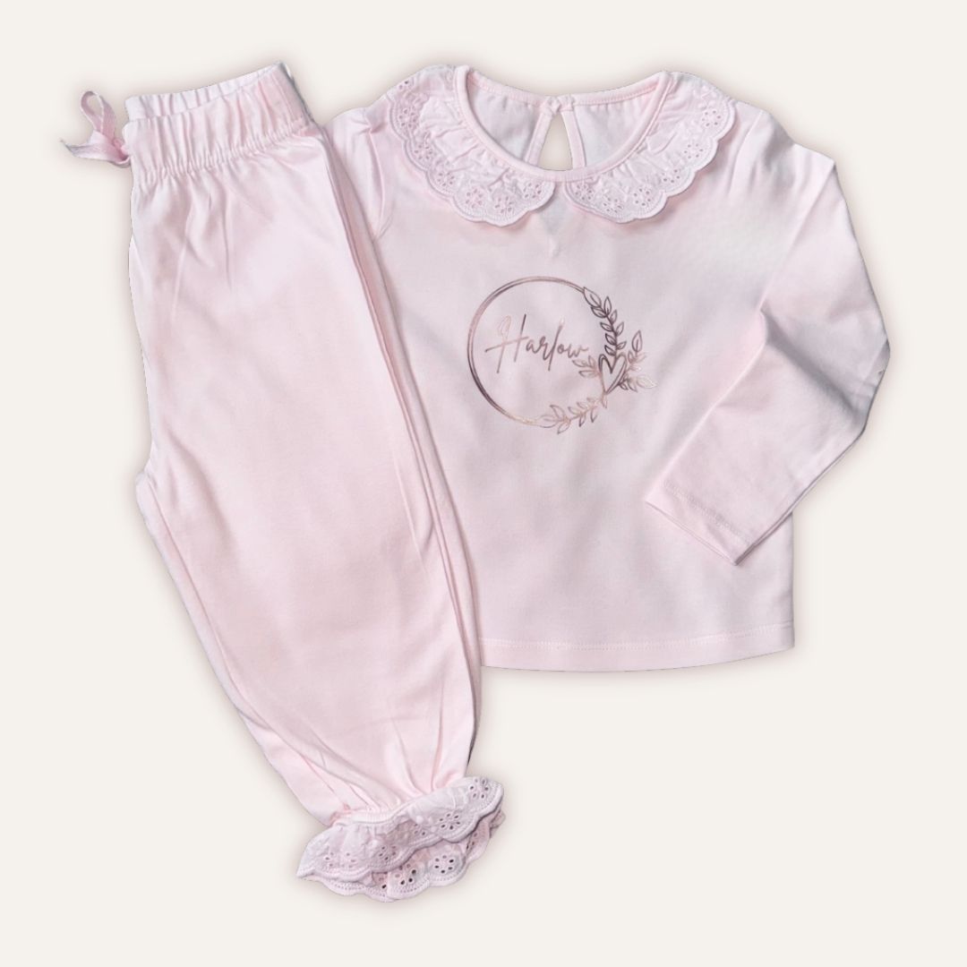 Pastel pink personalised broderie frill pyjamas with a rose gold wreath design, laid flat, Grace & Grayson