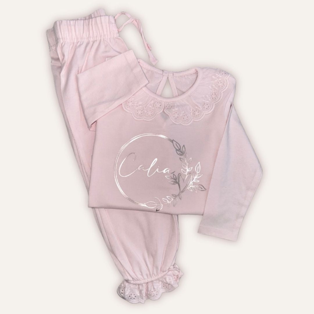 Pastel pink personalised broderie frill pyjamas with a silver wreath design, laid flat, Grace & Grayson
