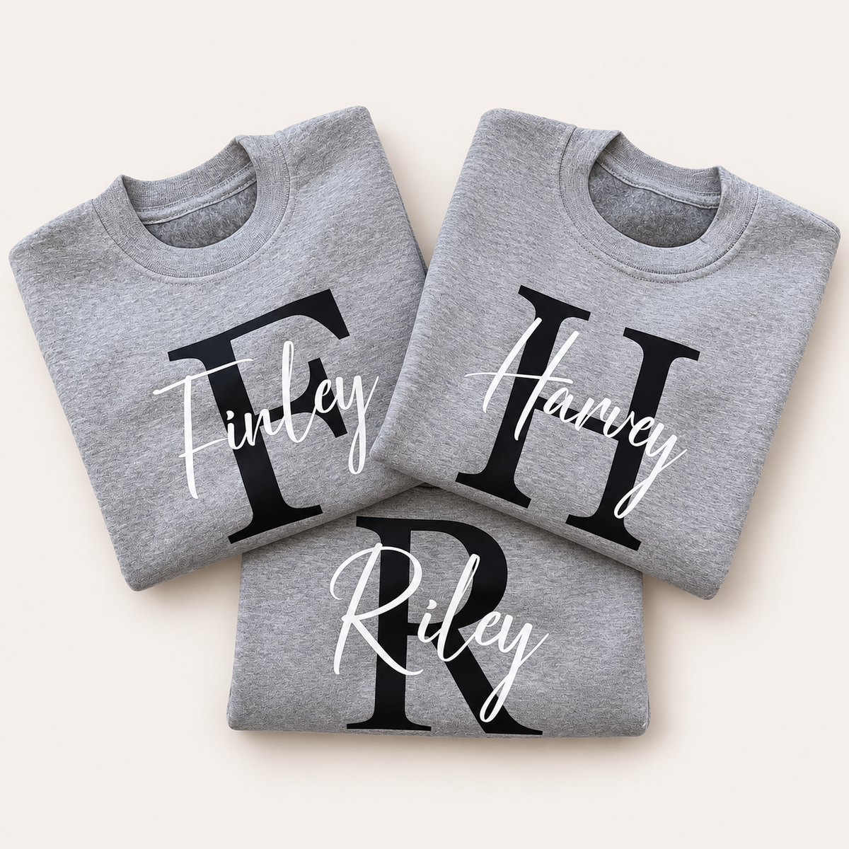 Three folded grey personalised sweatshirts with black initials and white script names | Grace & Grayson