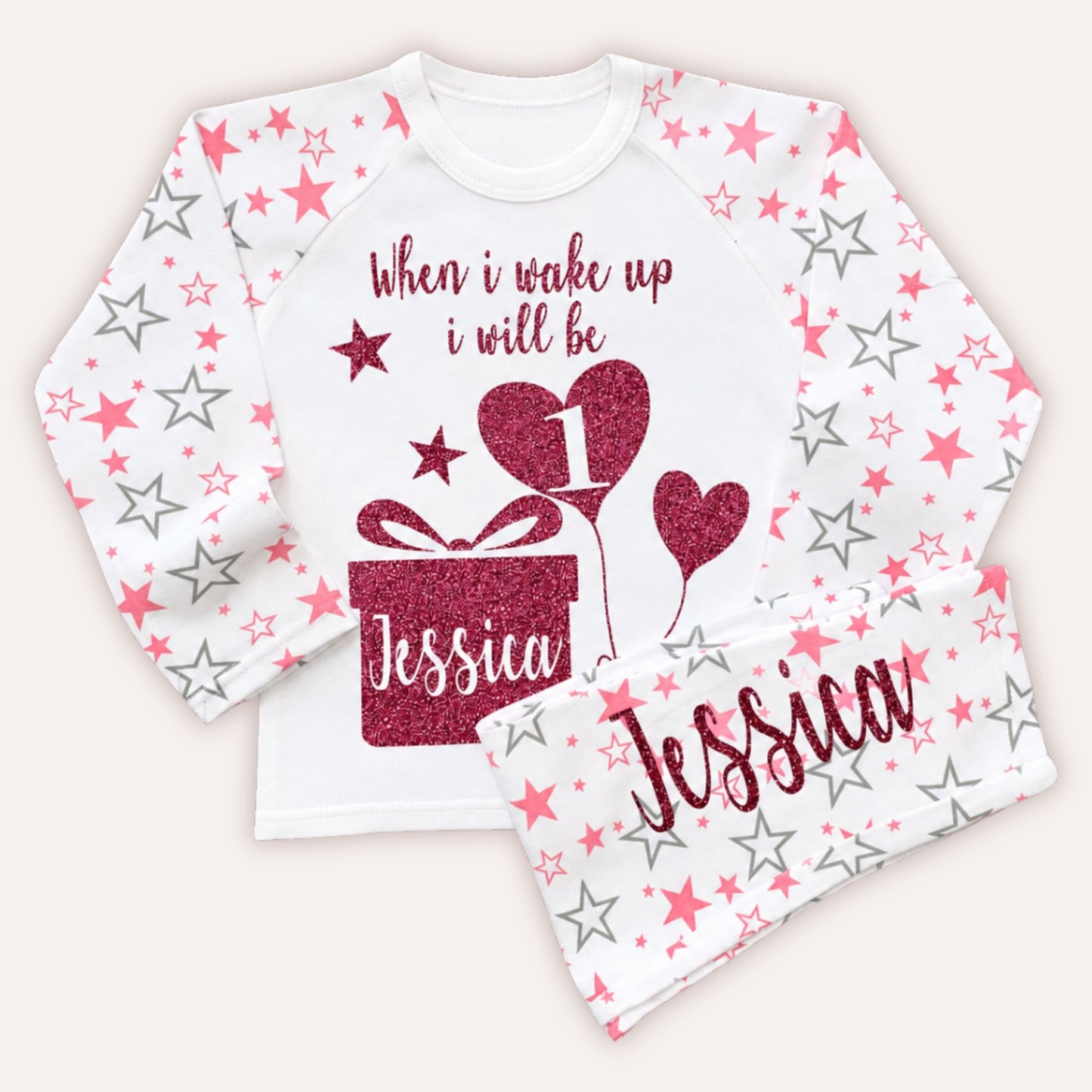 Personalised girls 1st birthday pyjamas with pink star print sleeves, glitter birthday design, gift box motif and custom name on matching pyjama bottoms.
