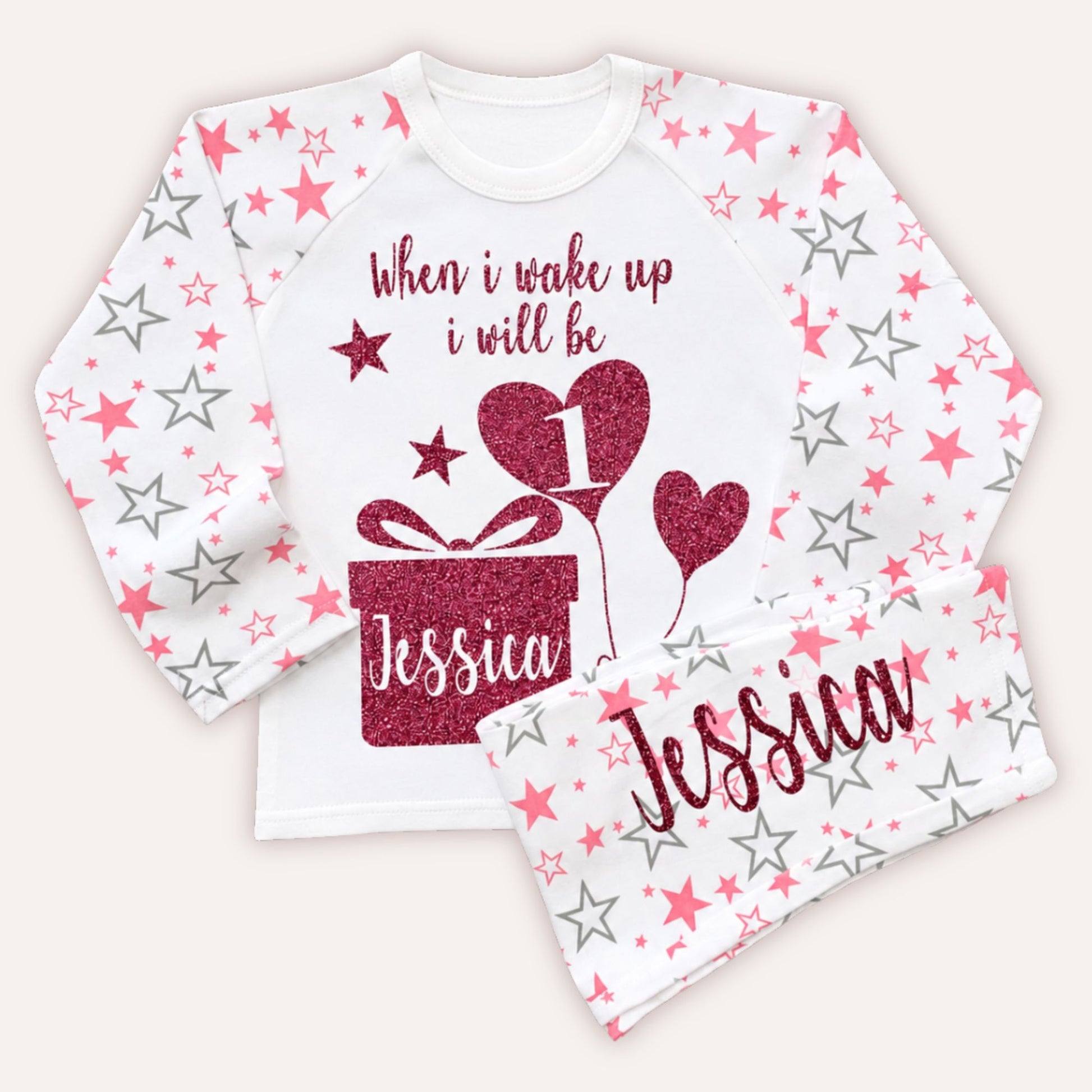Personalised girls 1st birthday pyjamas with pink star print sleeves, glitter birthday design, gift box motif and custom name on matching pyjama bottoms.