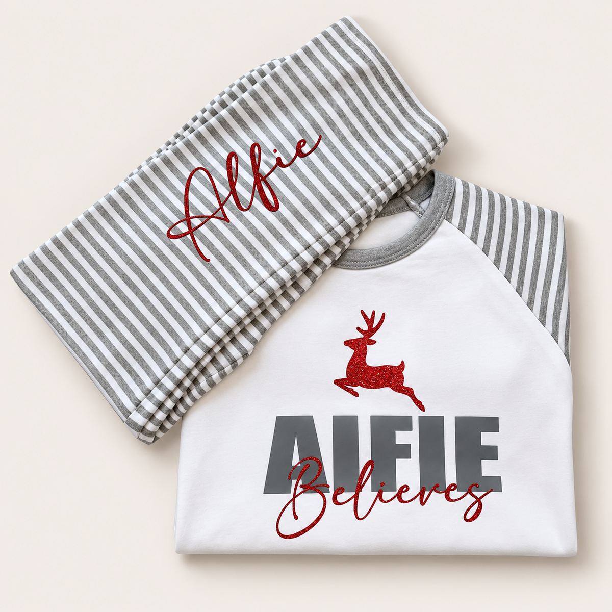 Personalised grey and white stripe Christmas pyjamas featuring a bold name, red reindeer and “Believes” design by Grace & Grayson