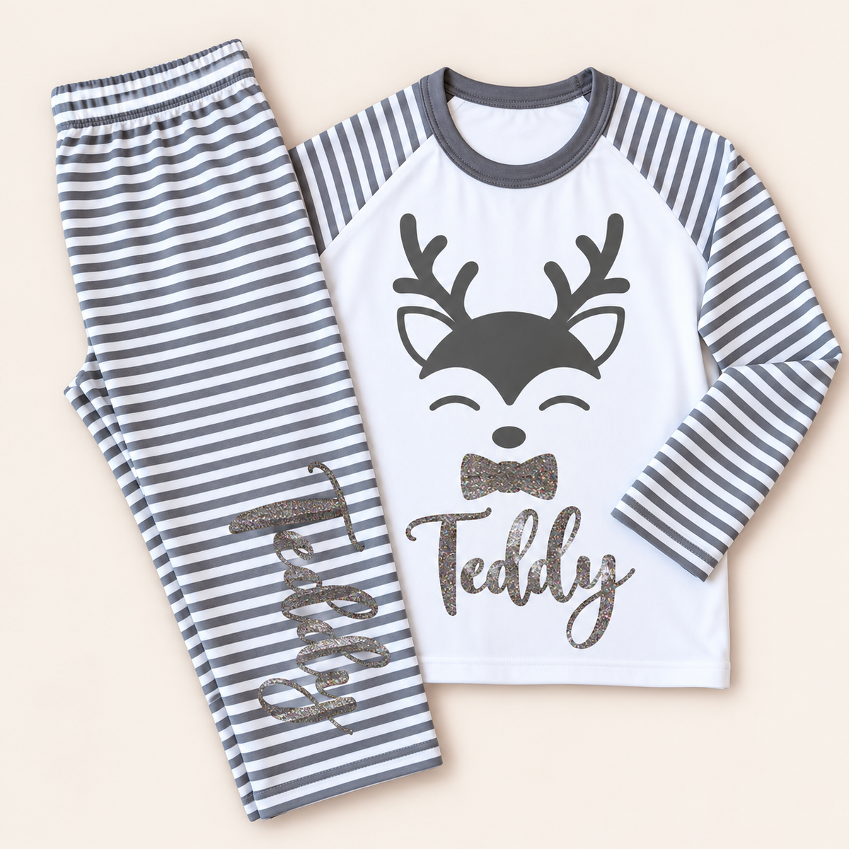 Personalised grey stripe Christmas reindeer pyjamas laid flat with a glitter reindeer design and bow, Grace & Grayson