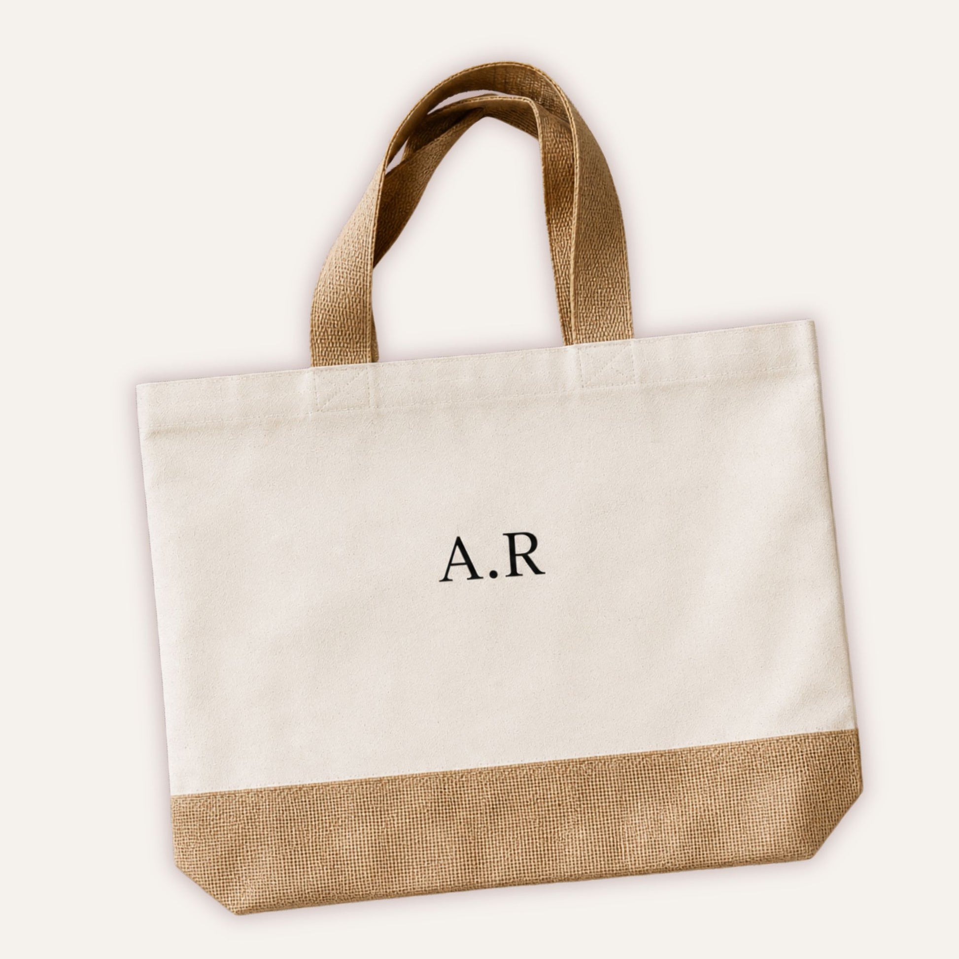 Personalised initials jute tote bag with custom monogram in classic serif font on cream canvas, shown at angle with natural jute base and handles | Grace & Grayson