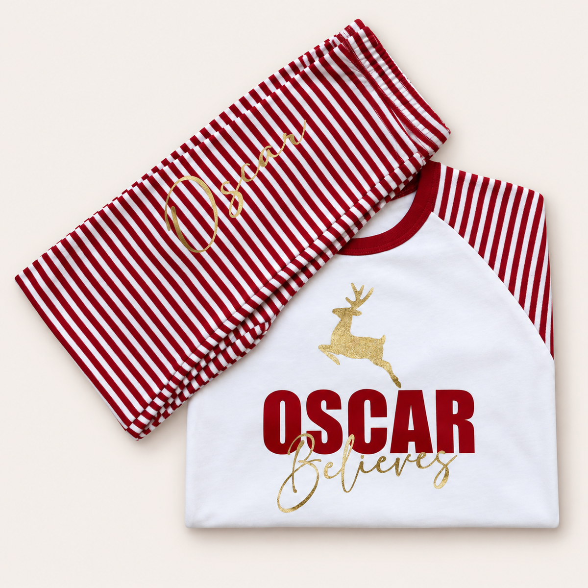 Personalised red and white striped Christmas pyjamas with gold reindeer, bold name and “Believes” design by Grace & Grayson