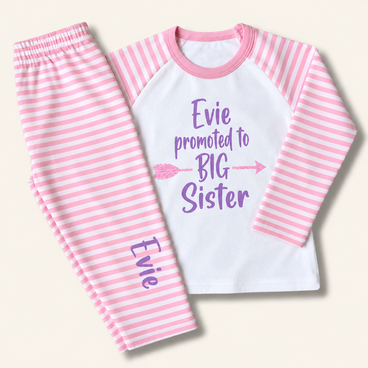 Pink and white striped personalised children’s pyjamas with a purple “Promoted to Big Sister” design, displayed flat, Grace & Grayson.