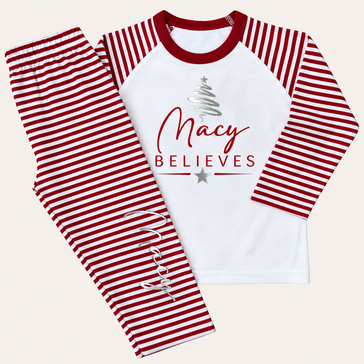 Red and white striped personalised Believes Christmas pyjamas with a silver Christmas tree design and red BELIEVES lettering, displayed flat, Grace & Grayson