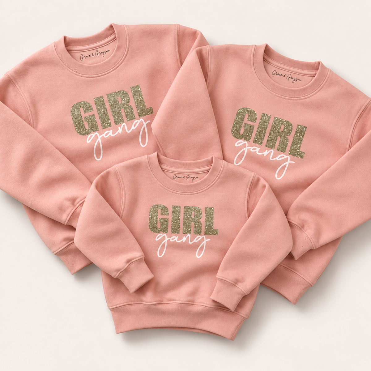 Three dusty pink Girl Gang sweatshirts arranged flat with glitter lettering and white script, Grace & Grayson