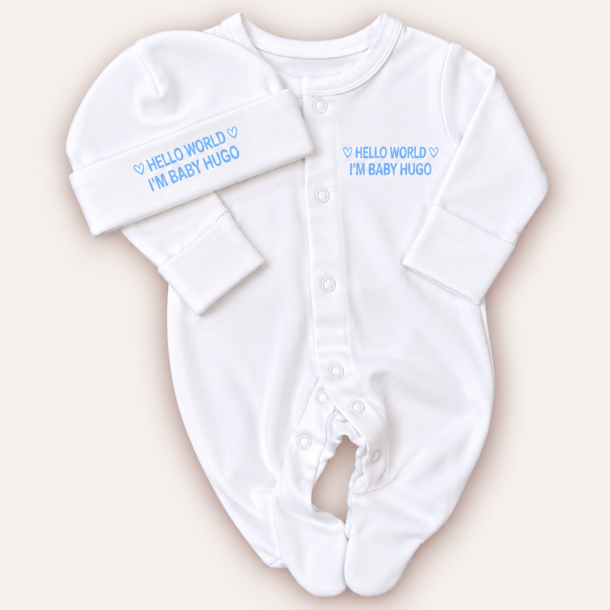 White personalised Hello World baby grow and matching hat with blue lettering and heart details, Grace & Grayson