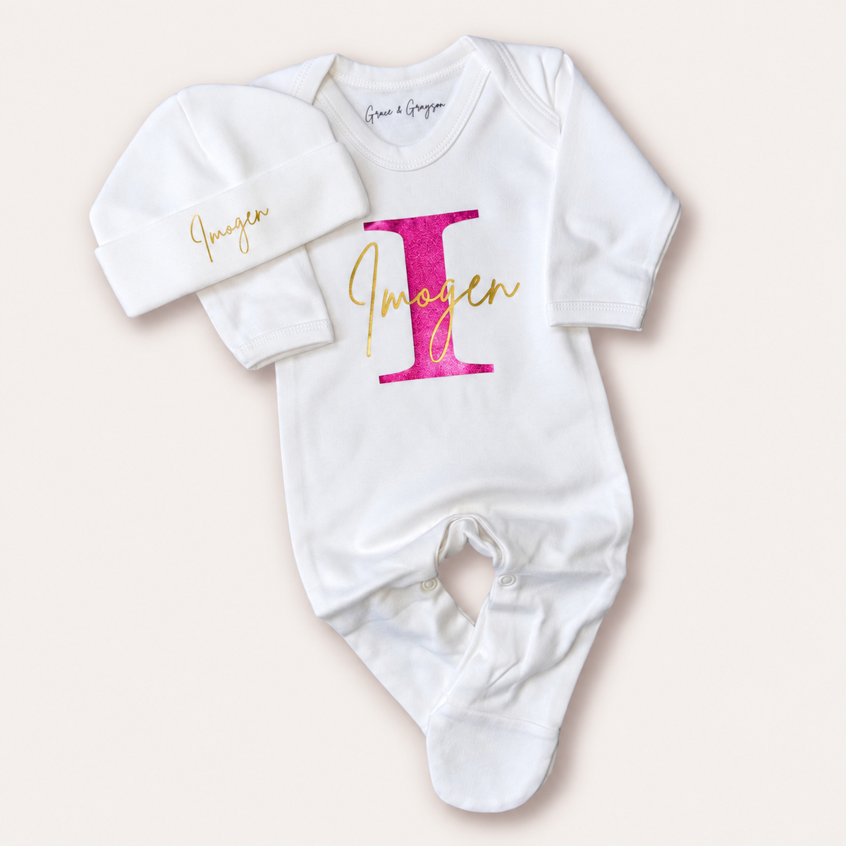 White personalised baby grow and matching hat with a pink and gold initial design, Grace & Grayson