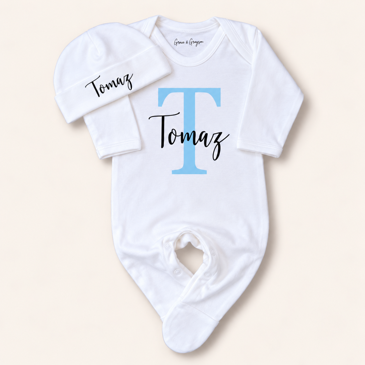 White personalised baby grow with a blue initial and matching hat, shown on a white background, Grace & Grayson
