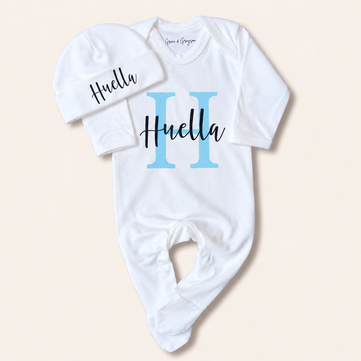 White personalised baby grow with a blue initial design, shown from the front, Grace & Grayson