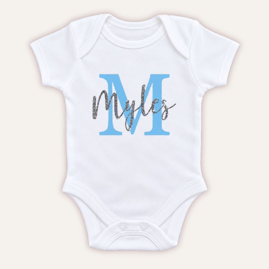 White personalised baby vest with a large blue initial and silver glitter script name, displayed on a light background, Grace & Grayson.