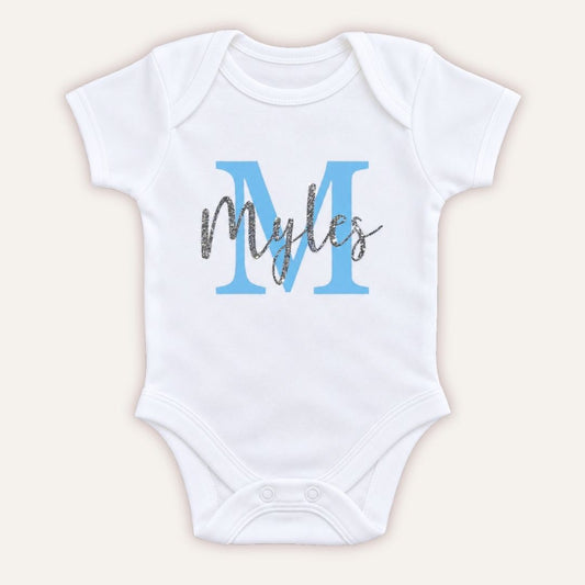 White personalised baby vest with a large blue initial and silver glitter script name, displayed on a light background, Grace & Grayson.