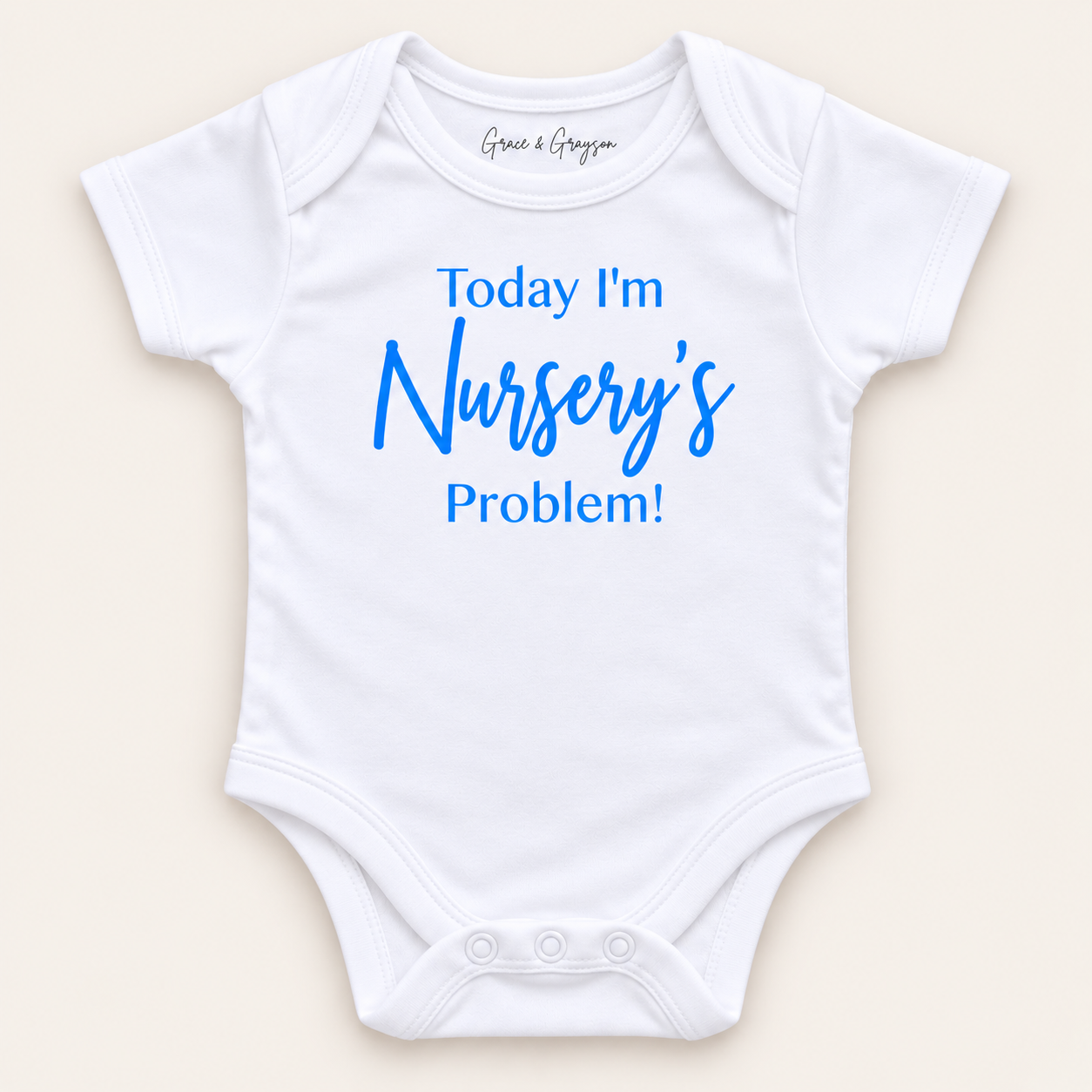 White personalised baby vest with blue lettering reading “Today I’m Nursery’s Problem!”, displayed on a light background, Grace & Grayson.