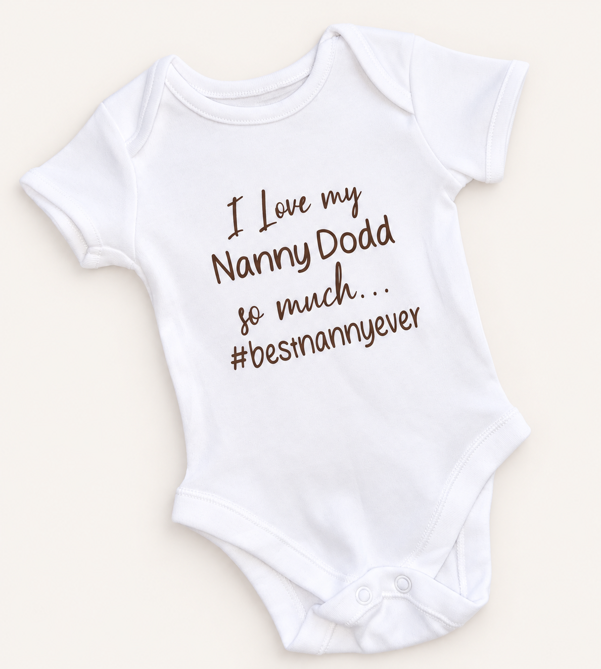White personalised baby vest with brown lettering featuring a funny family message and the hashtag #bestnannyever, displayed on a light background, Grace & Grayson.