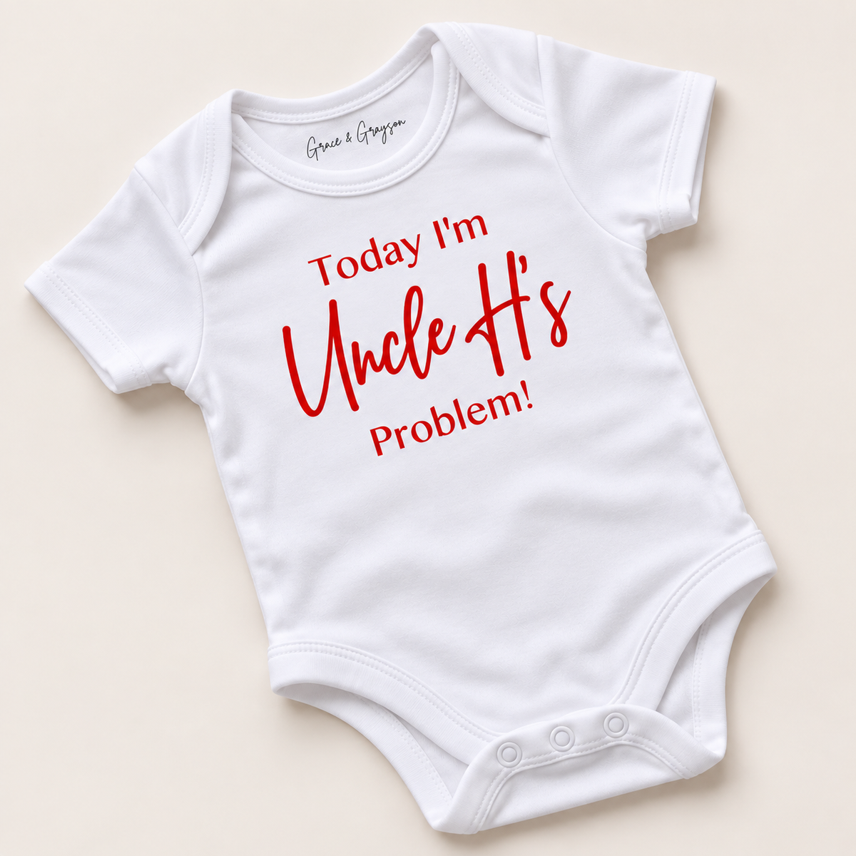 White personalised baby vest with red lettering reading “Today I’m Uncle’s Problem!”, displayed at an angle on a light background, Grace & Grayson