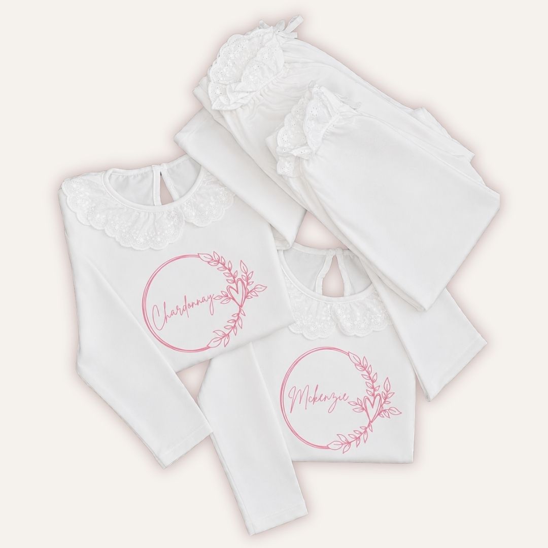 White personalised broderie frill pyjamas with pink wreath designs, displayed as a coordinated set, Grace & Grayson