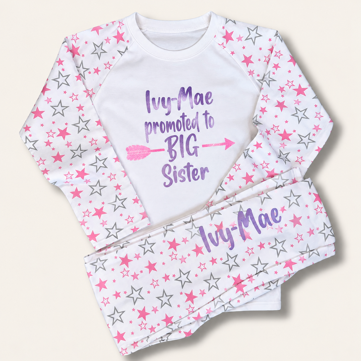 White personalised children’s pyjamas with pink and grey star-print sleeves and trousers, featuring a “Promoted to Big Sister” design, Grace & Grayson.