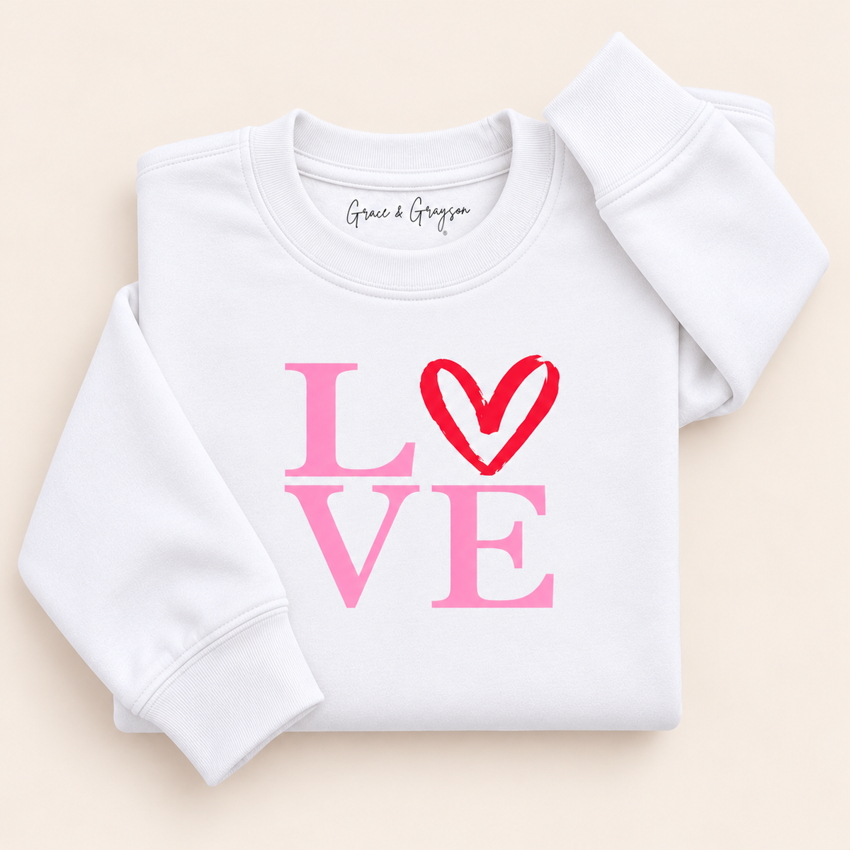 White sweatshirt with pink LOVE lettering and a red heart replacing the O, folded on a cream background | Grace & Grayson