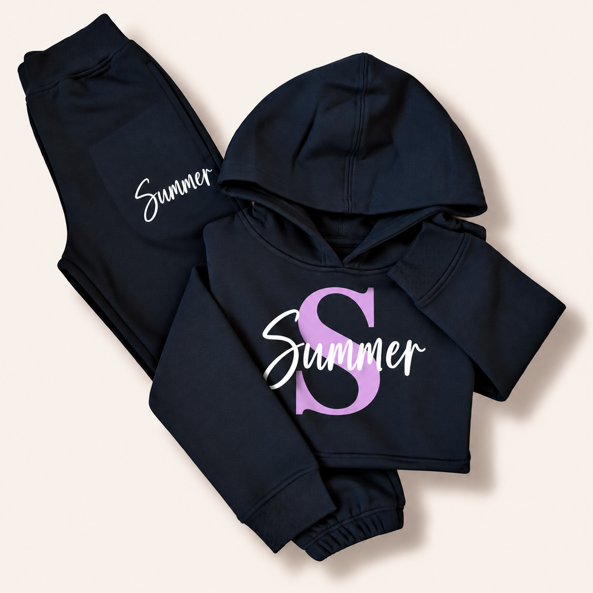 Navy folded hoodie tracksuit with a lilac initial and white script name personalisation, laid flat on a cream background. Grace & Grayson